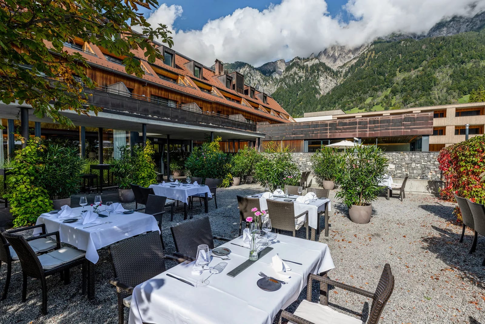 Weiss gedeckte Tische auf Kies, dahinter ragen die Berge über die Wolken: die Terrasse des Hotels Traube Braz.